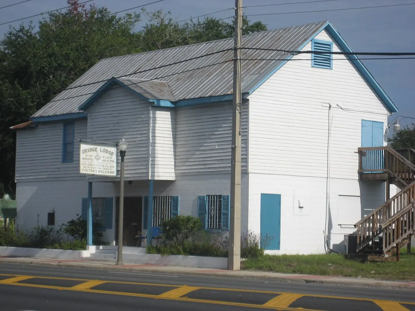 White two-story wooden lodge building with blue shutters on an Apopka street