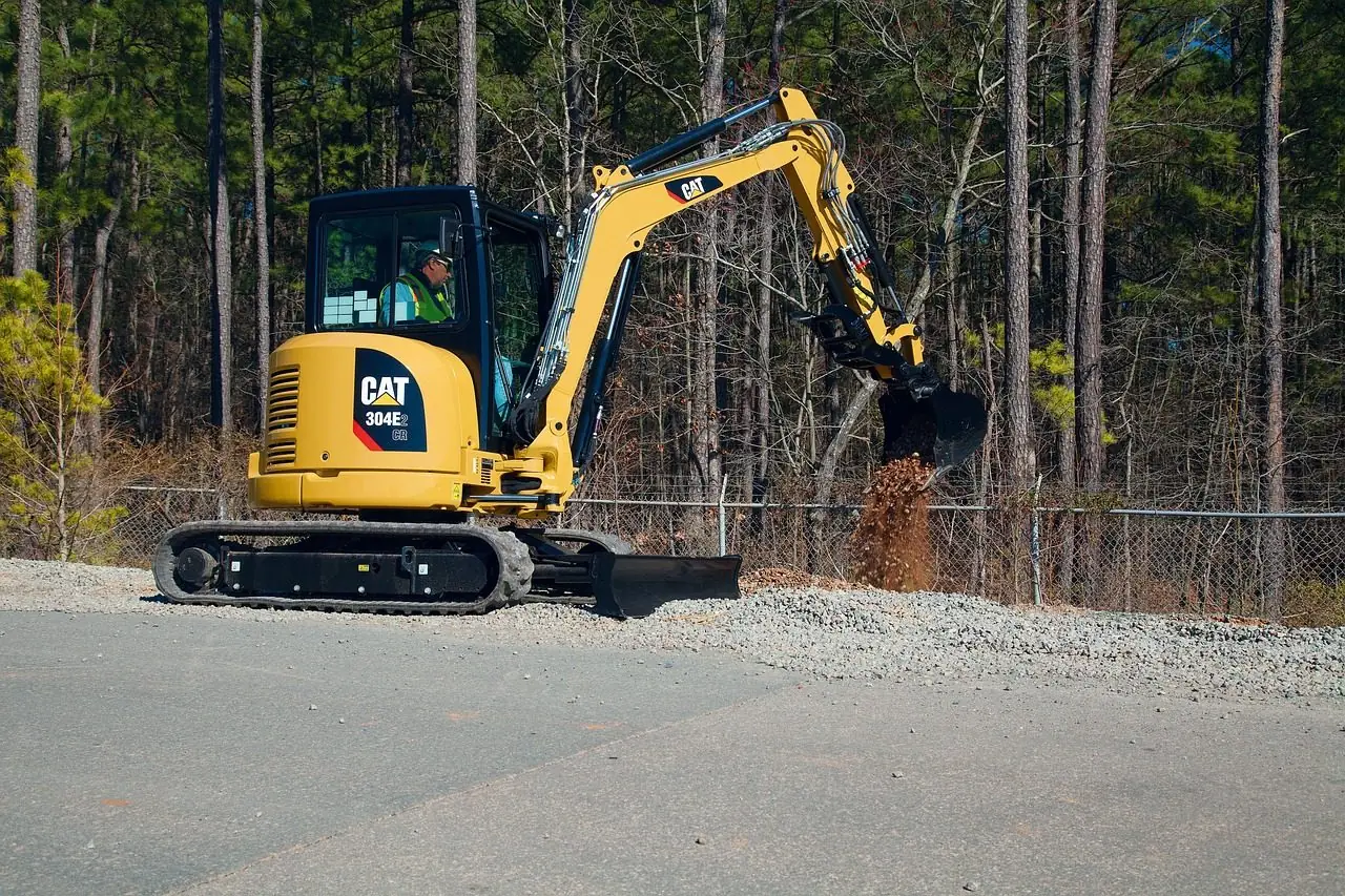 Compact excavator digging at the edge of a wooded lot